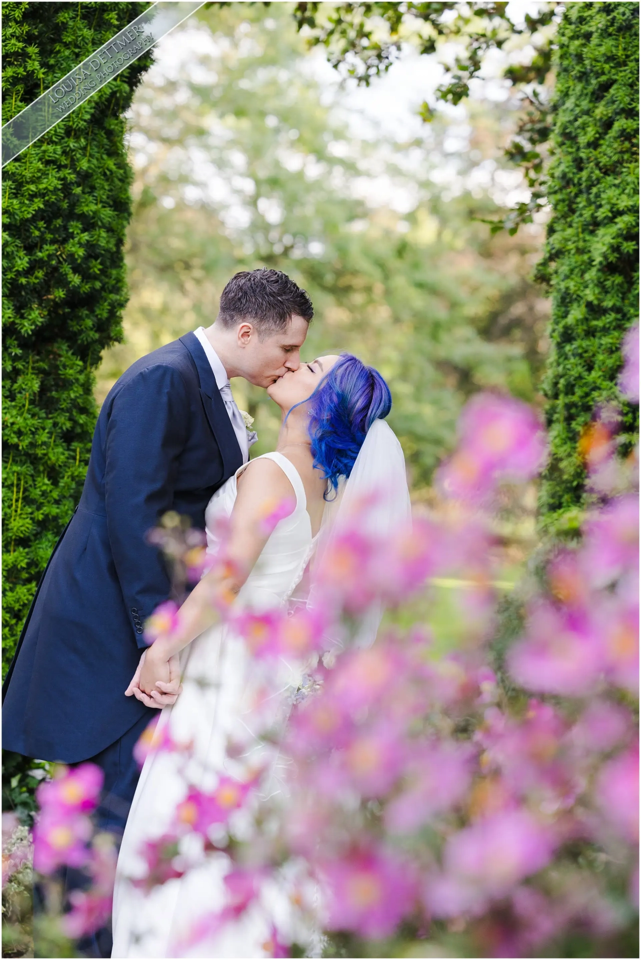 bride and groom kissing, pink flowers, blue hair, at the Orangery Maidstone by Kent Photographer Louisa Dettmer Photography