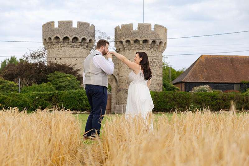 bride and groom kissing, holding hands, kissing brides hand, dancing in long grass and corn field at Cooling Castle Barn Wedding Venue by Louisa Dettmer Photography