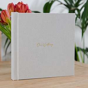 A gray hardcover album with gold script on the cover sits on a wooden table, with red tulips and green plants in the background.