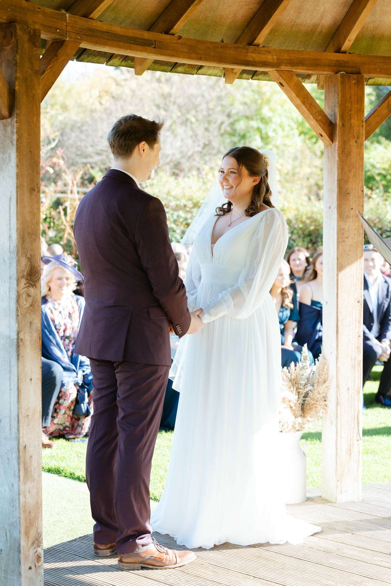 Bride and groom holding hands under a wooden gazebo at an outdoor wedding ceremony.