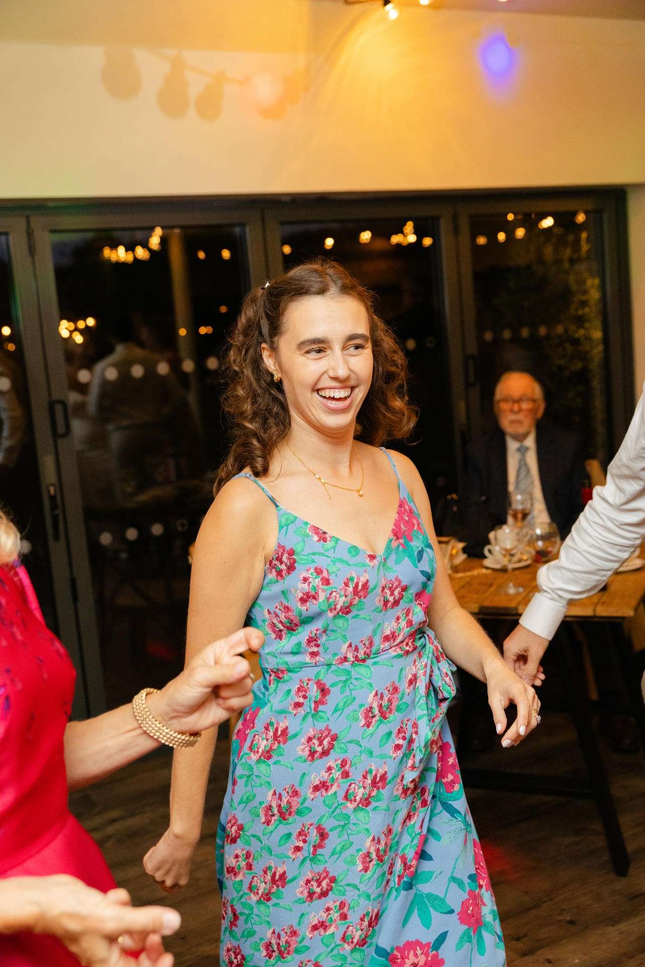 A woman in a blue floral dress dancing and laughing at a party.