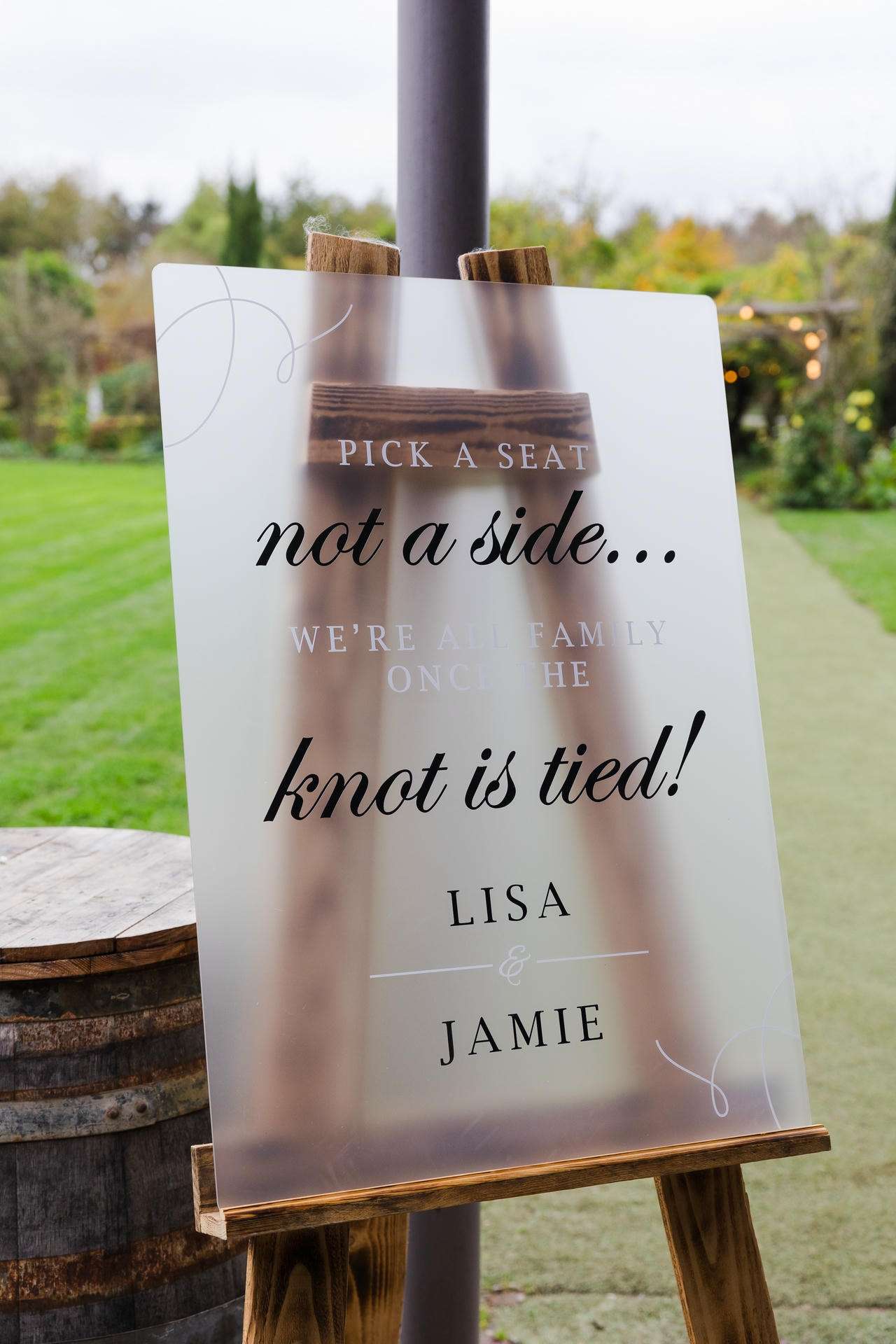 Outdoor wedding sign on a wooden easel that reads “Pick a seat, not a side… the knot is tied!” with the names Lisa and Jamie.