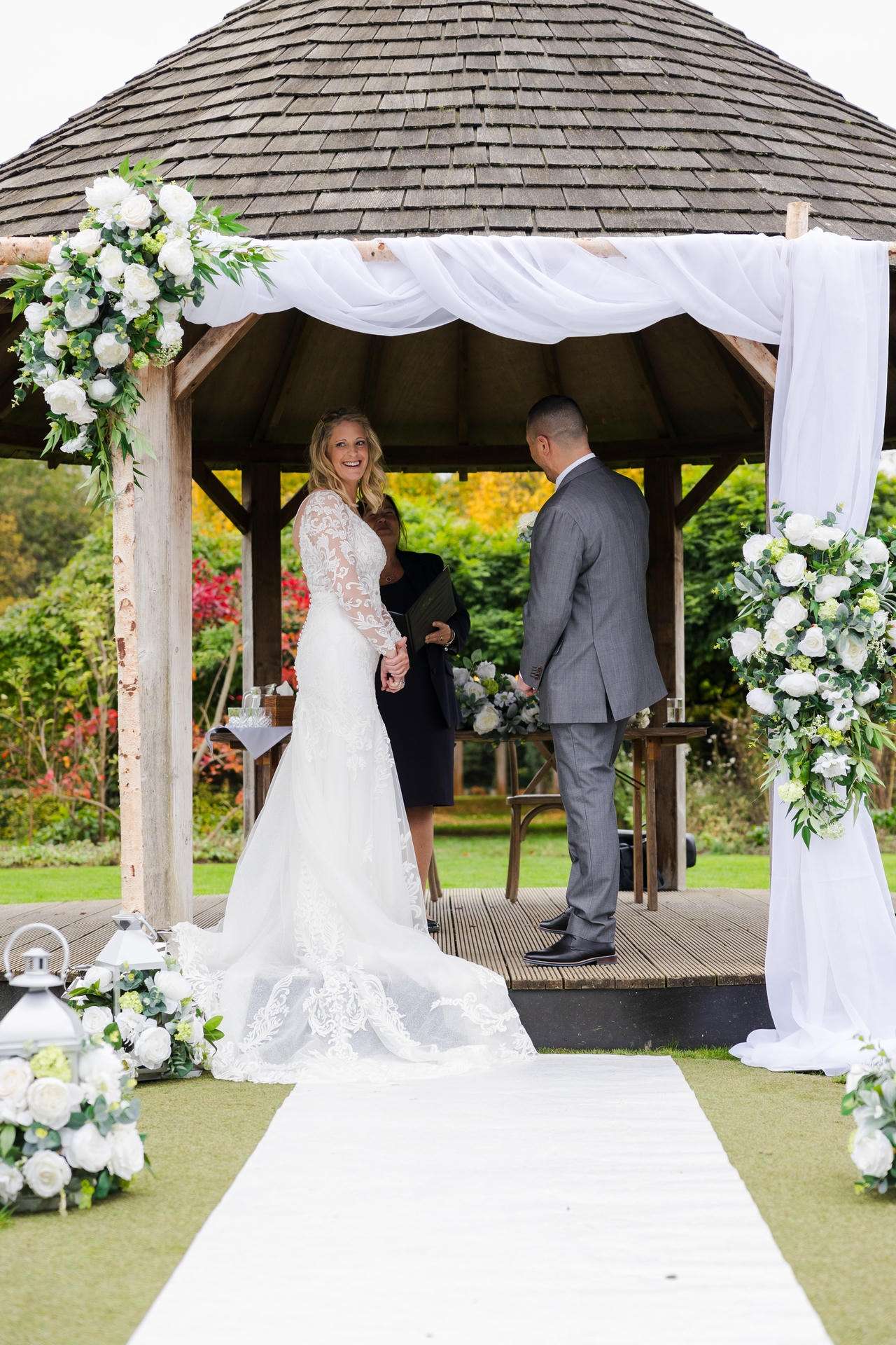 Bride and groom stand under a white-draped, flower-decorated gazebo at an outdoor wedding.