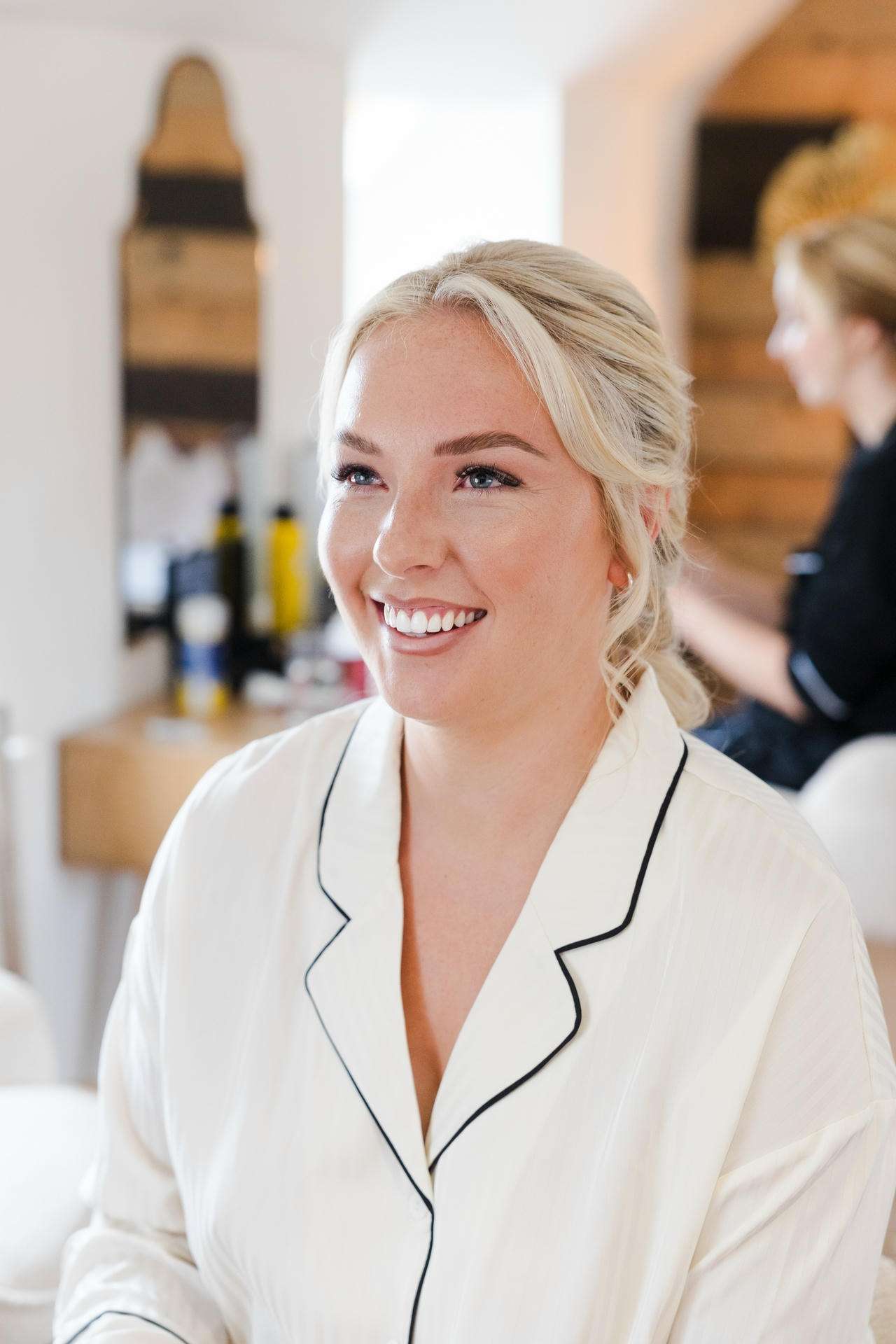 Smiling blonde woman in a white robe with black piping, indoors.