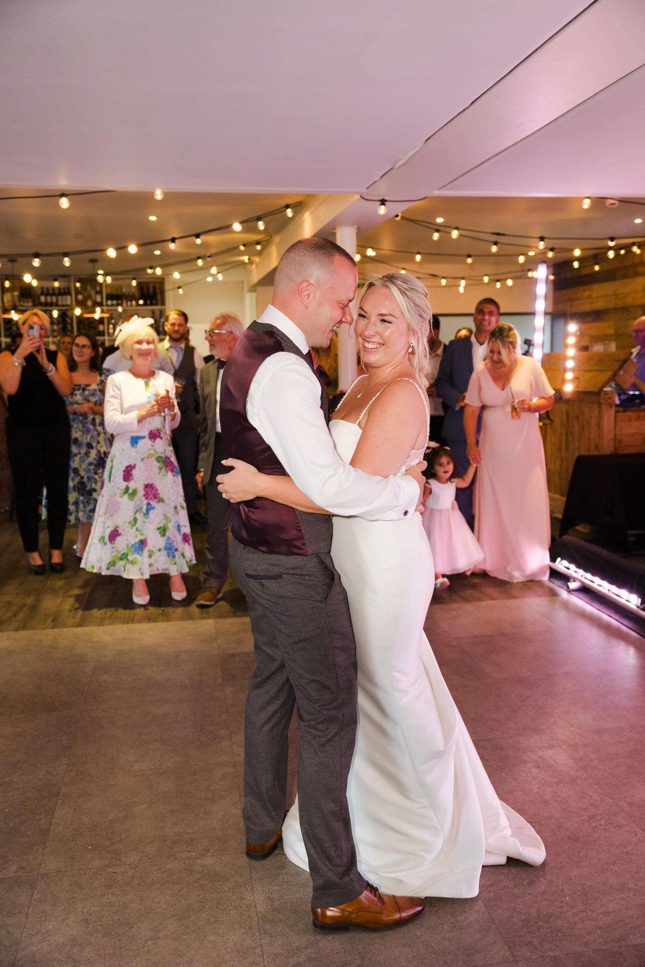 Bride and groom dance together at their wedding reception as guests watch.
