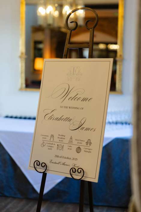 Elegant wedding welcome sign on an easel reading "Welcome to the wedding of Elisabetta James" in a reception room.