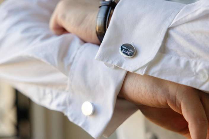 Close-up of a silver round pin badge on the cuff of a white shirt.