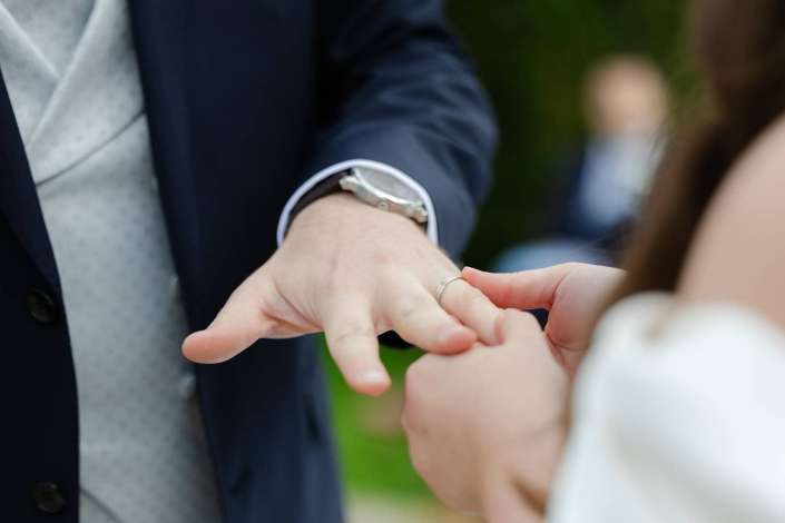 Close-up of two hands during a ring exchange, one wrist wearing a silver watch.