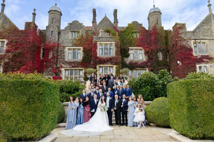 Bride and groom with a large wedding party posing on the steps of an ivy-covered stone mansion.