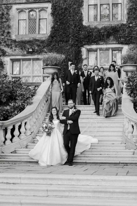 Bride and groom lead their wedding party down a grand stone staircase in front of an ivy-covered building.