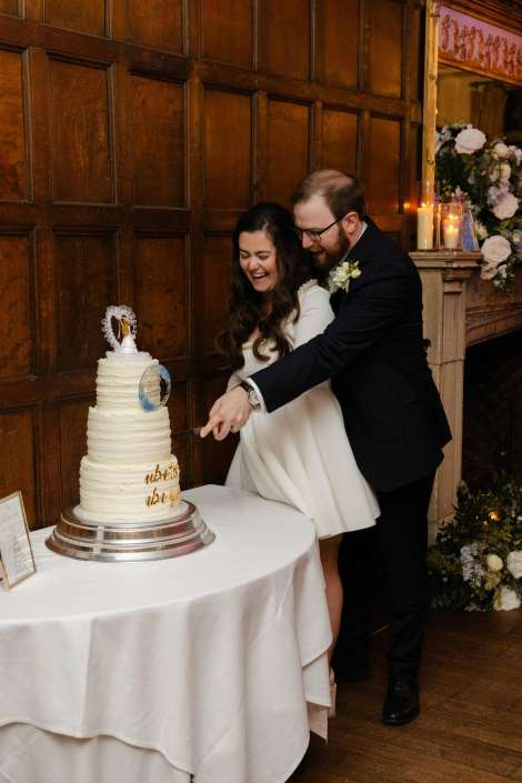 Bride and groom cut a tall white multi-tier wedding cake together at their reception.