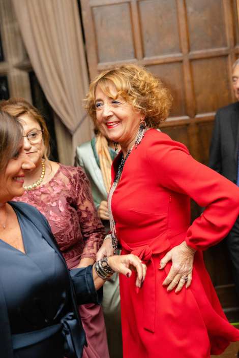 Smiling woman in a bright red dress dancing with guests at a formal indoor party.