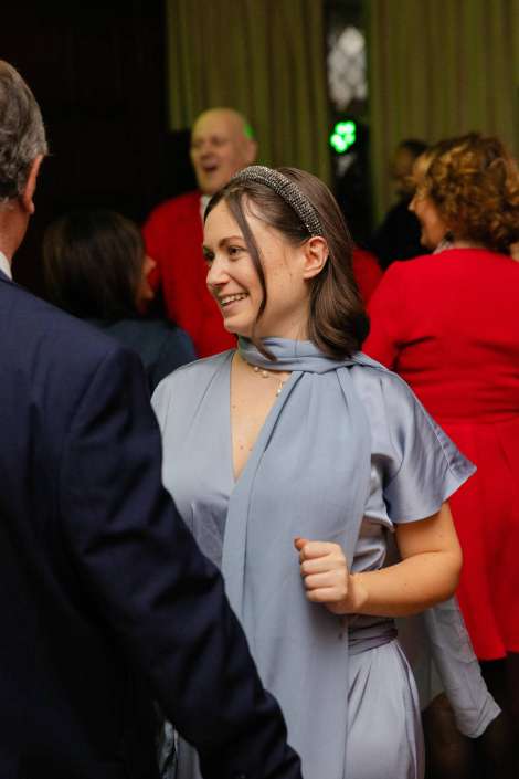 Smiling young woman in a light blue dress with a silver headband at a social event, with others wearing red in the background.
