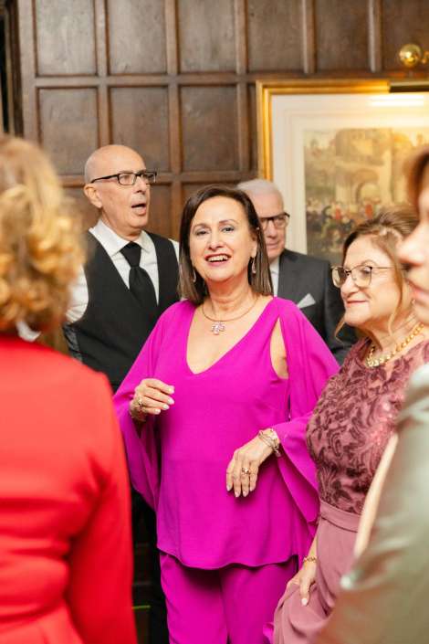 Smiling woman in a bright magenta outfit stands among formally dressed guests at a social event.