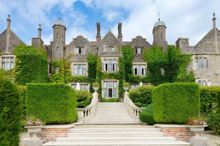 ivied mansion grand staircase Stately ivy-covered stone mansion with tall chimneys, arched windows, and a wide central staircase leading to the entrance.