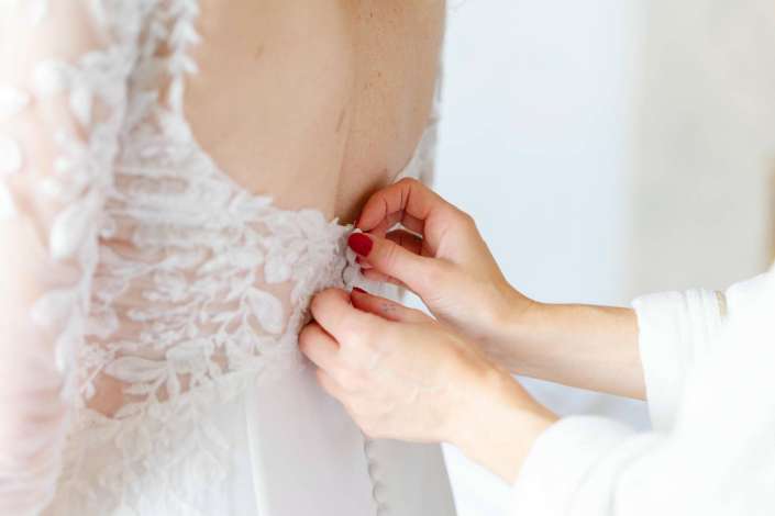 buttoning a lace wedding dress Close-up of hands fastening the buttons along the back of a white lace wedding dress.