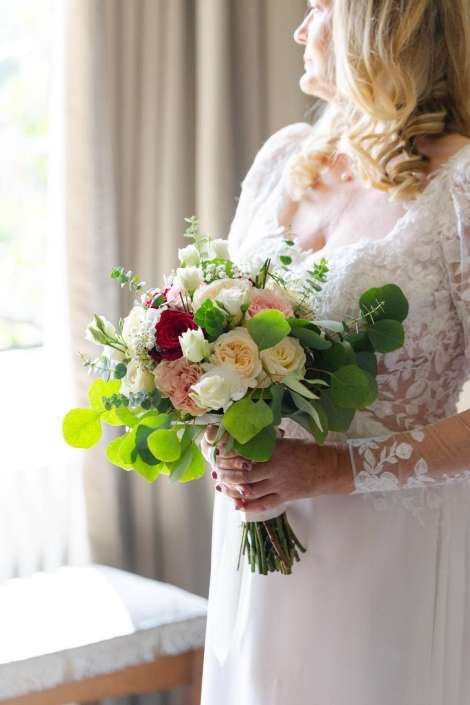 bridal bouquet with roses Bride in a lace wedding dress holding a bouquet of white, blush, and red roses with green foliage.
