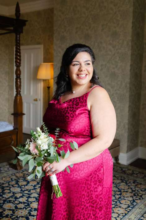 smiling woman in pink leopard dress Smiling woman in a pink leopard-print dress holds a bouquet of white and pink flowers with greenery indoors.
