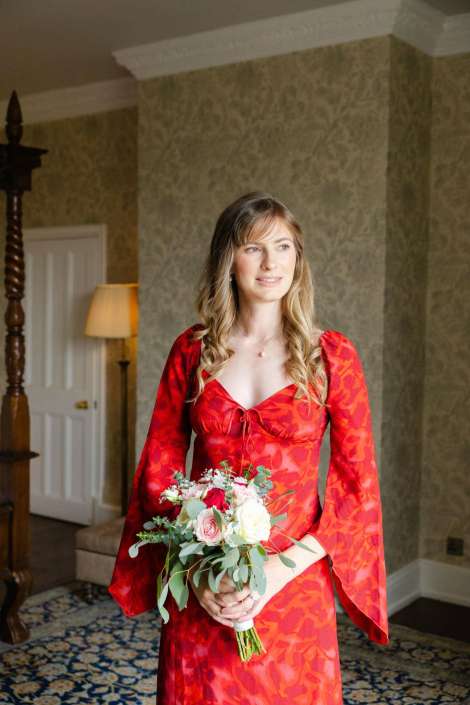 red dress bride with bouquet A woman in a red patterned dress holds a bouquet of pink and white roses with greenery indoors.