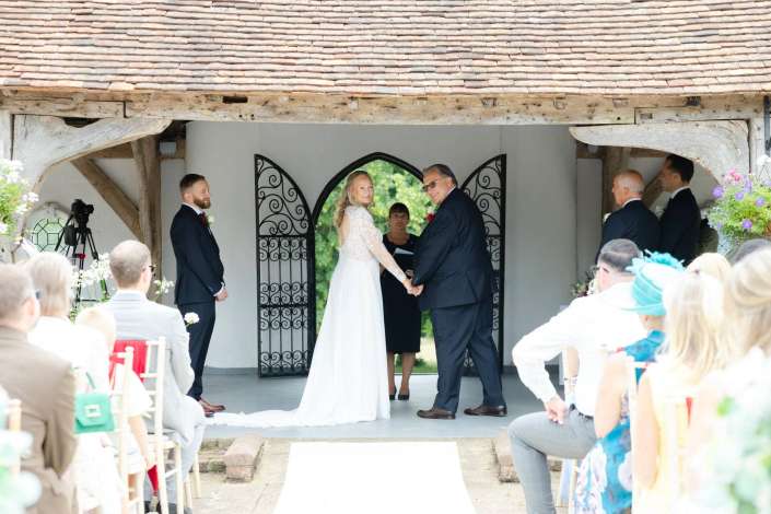 bride and groom exchange vows Bride and groom hold hands at the altar of a rustic open-air chapel as guests look on.