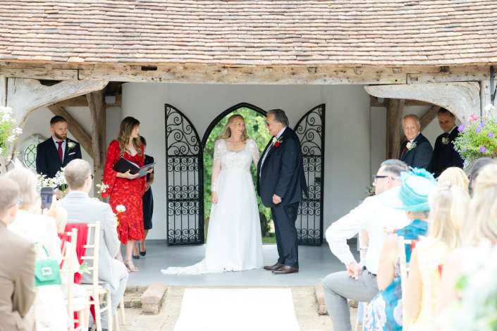 bride and groom exchange vows Bride and groom stand facing each other under an arched doorway with wrought-iron panels during an outdoor wedding, as guests sit on both sides.