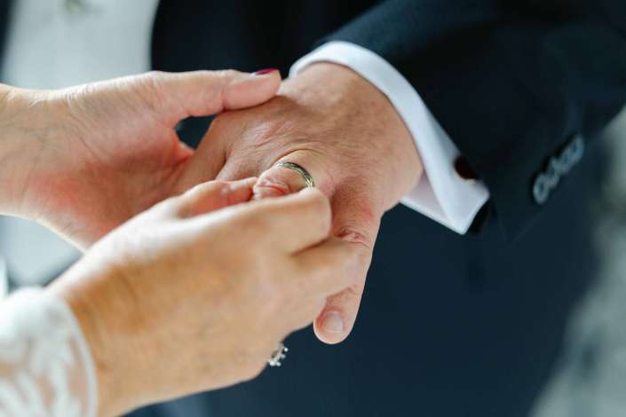 wedding ring exchange Close-up of hands placing a silver wedding band on a partner's finger during a wedding ceremony.
