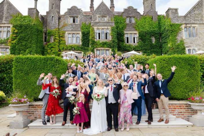 wedding party at ivy mansion Bride and groom with a large group of wedding guests posing on steps in front of an ivy-covered stone mansion.