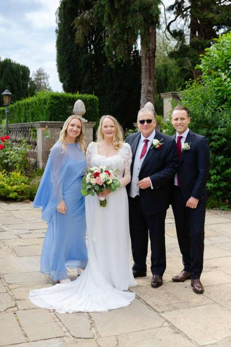 elegant garden wedding portrait Bride in a white gown holding a bouquet stands with two men in suits and a woman in a light blue dress in a garden.
