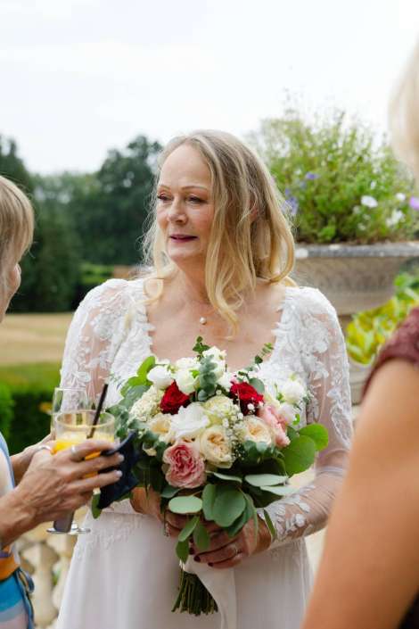 bride holding floral bouquet Bride in a lace wedding dress holding a bouquet of white, pink, and red roses with greenery outdoors.