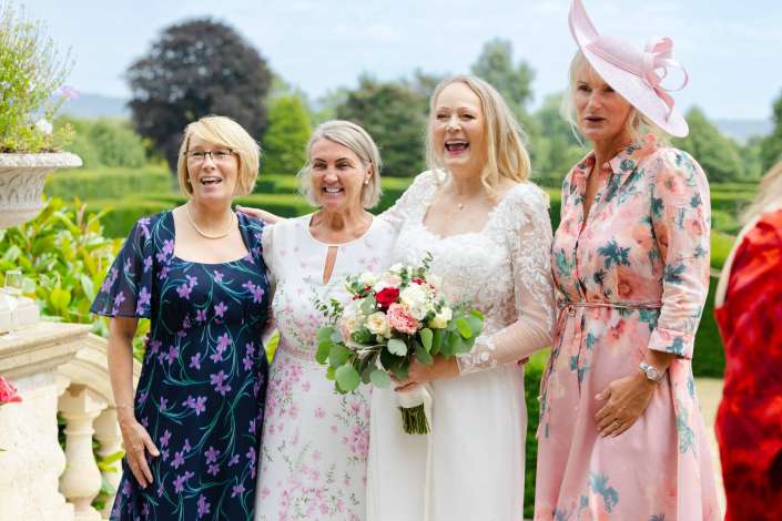 bride and friends at garden wedding Bride in a white lace dress holding a bouquet stands with three women in floral dresses outdoors at a garden wedding.