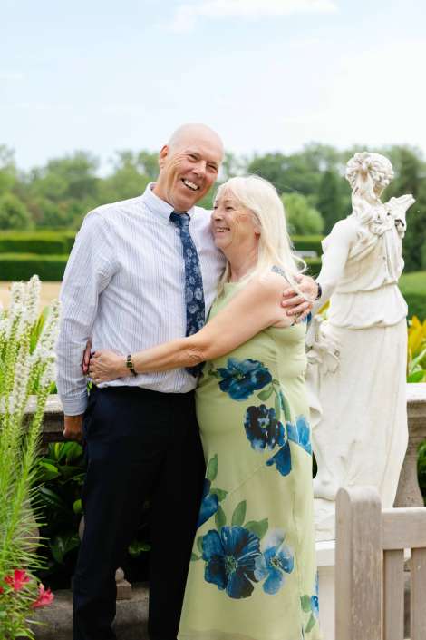 joyful couple in garden A smiling elderly couple hugs in a garden with a white statue in the background.