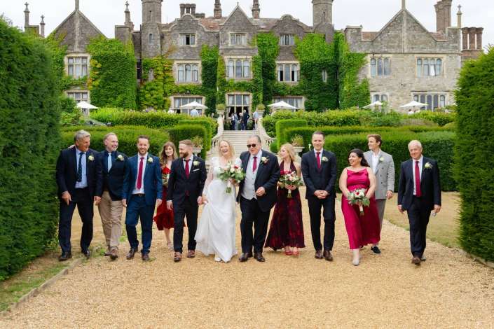 bridal party at historic estate Bride and wedding party walk along a gravel path in front of an ivy-covered historic manor.