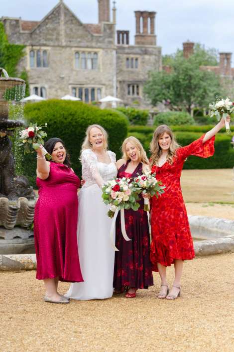 wedding party by fountain Bride and three bridesmaids posing with bouquets in front of a historic stone mansion and fountain.