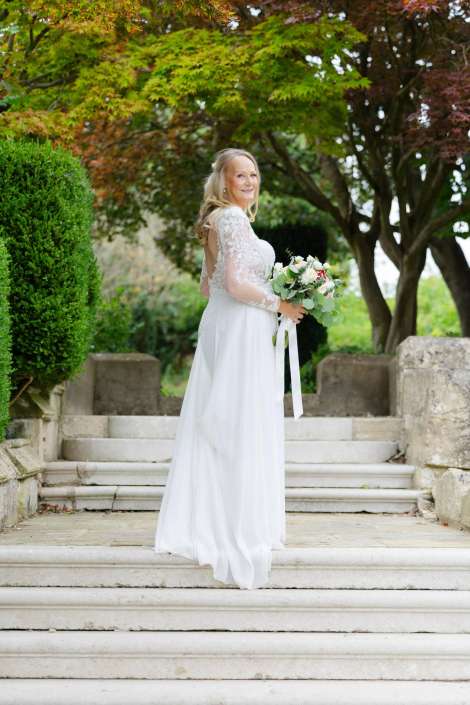 bridal portrait on stone steps Bride in a white lace gown stands on stone steps holding a bouquet among green and autumn foliage. Photo by Louisa Dettmer Wedding Photography, Kent Wedding Photographer