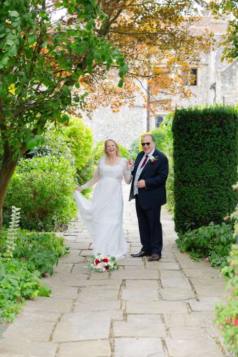 bride and groom garden stroll Bride in a white wedding dress and her groom in a dark suit walk arm in arm along a stone garden path, smiling, with a bouquet laid on the path.