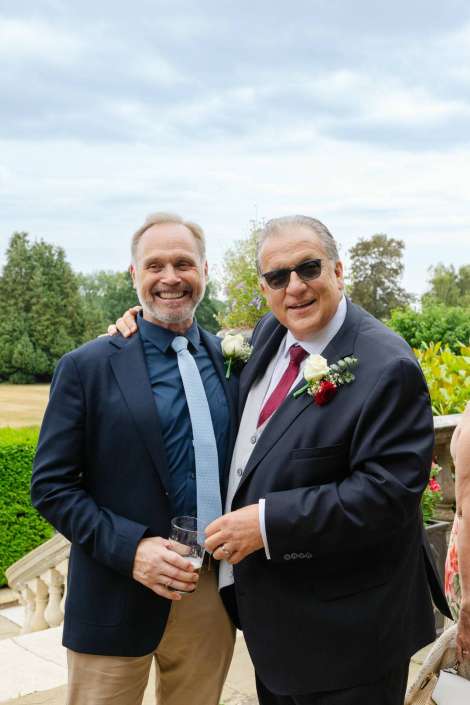 two men at outdoor wedding Two men in suits pose together at an outdoor wedding, smiling at the camera.