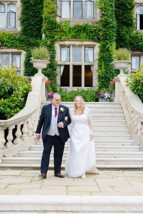 bride and groom on stairs A bride in a white lace wedding dress and a groom in a dark suit walk arm in arm down a stone staircase in front of an ivy-covered building.
