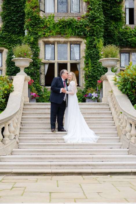 ivy covered staircase wedding kiss Bride in a white gown and groom in a dark suit kiss on a grand stone staircase outside an ivy-covered building with flowering planters. Photo by Louisa Dettmer Wedding Photography, Kent Wedding Photographer