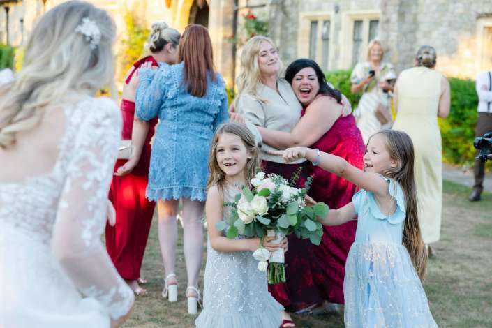 flower girls at outdoor wedding Two young girls in light blue dresses hold bouquets and smile at an outdoor wedding with guests in colorful outfits.