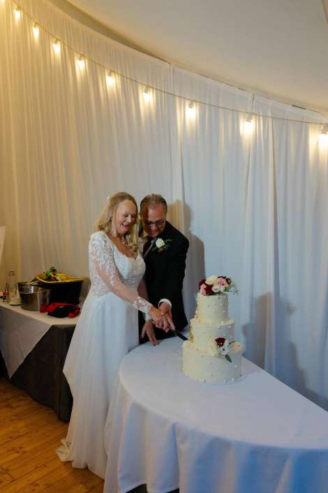 bride and groom cutting cake Bride and groom cutting a three-tier white wedding cake decorated with roses.