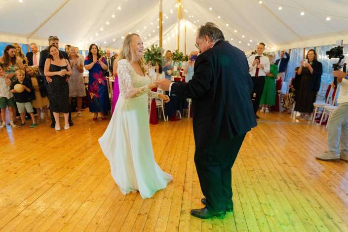 bride dancing under string lights Wedding dance celebration in marquee.