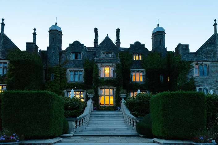 ivy covered castle at dusk Historic stone manor with ivy-covered walls, decorative chimneys, and warm light glowing from its windows sits at the top of a grand stone staircase. Photo by Louisa Dettmer Wedding Photography, Kent Wedding Photographer