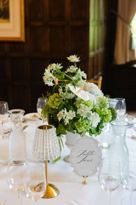white floral centerpiece on table White and green flower centerpiece on a dining table with glassware and a decorative "Table Four" place card.