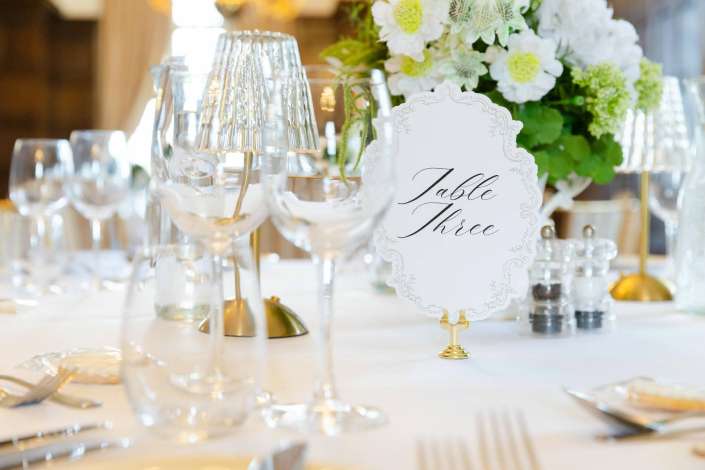 elegant table setting with flowers Elegant dining table with crystal glassware, a white floral centerpiece, and a decorative 'Table Three' sign.