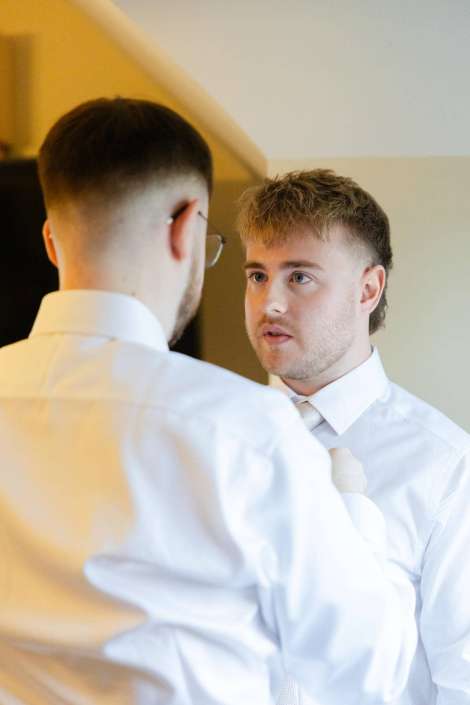 groom getting ready with best man A man in a white shirt and light tie has his tie adjusted by another man wearing a white shirt and glasses.