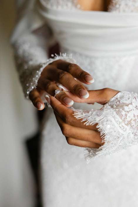 engagement ring moment Close-up of a bride's hands wearing a diamond engagement ring, with lace wedding dress sleeves.