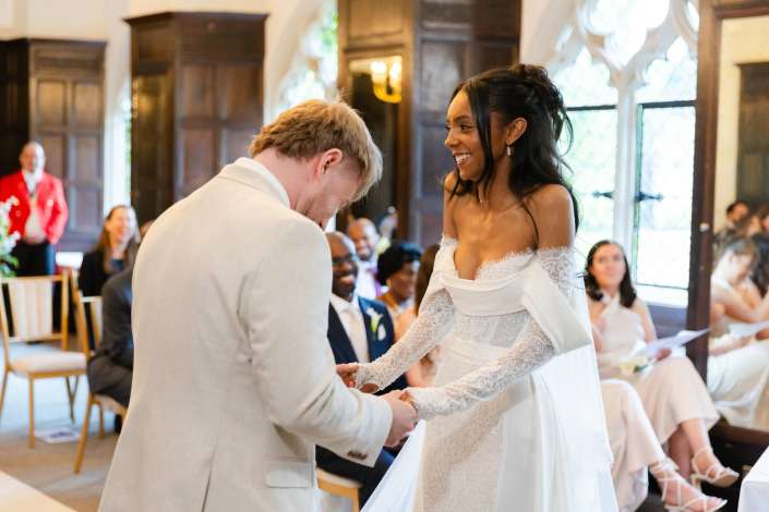bride and groom exchange rings Bride in a lace wedding gown and groom in a light suit exchange rings and smile during their wedding ceremony in a church.