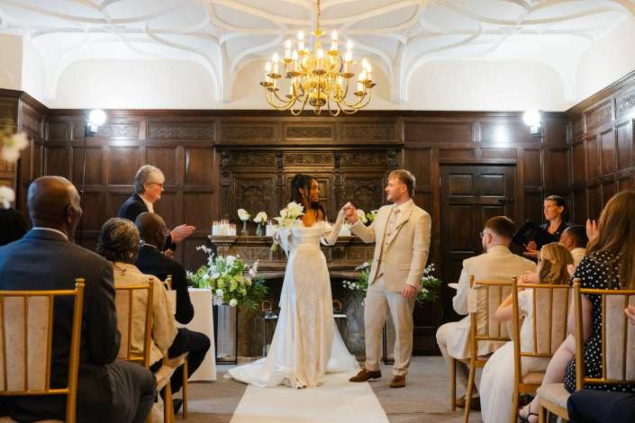 bride and groom exchange vows Bride and groom exchange rings during their wedding ceremony in a wood-paneled room with a gold chandelier overhead.