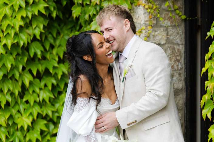 joyful bride and groom Bride and groom laughing and embracing outdoors beside an ivy-covered stone wall.