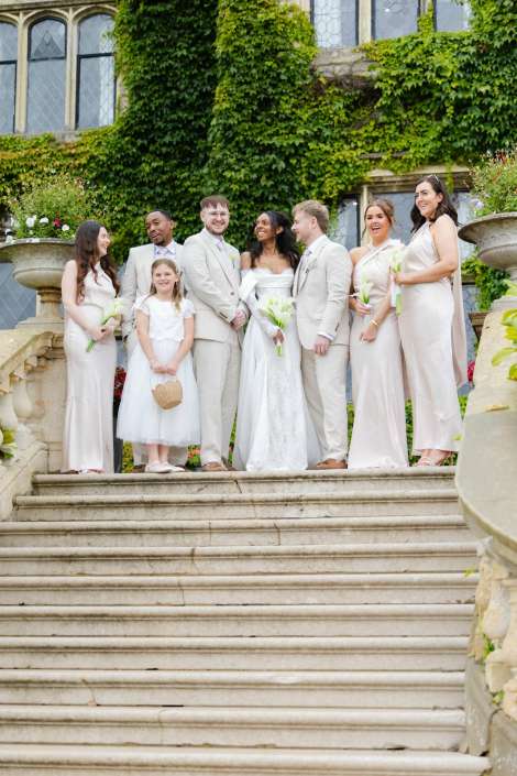bridal party on stone steps Bride and groom stand with bridesmaids, groomsmen, and a young flower girl on stone steps outside an ivy-covered building.